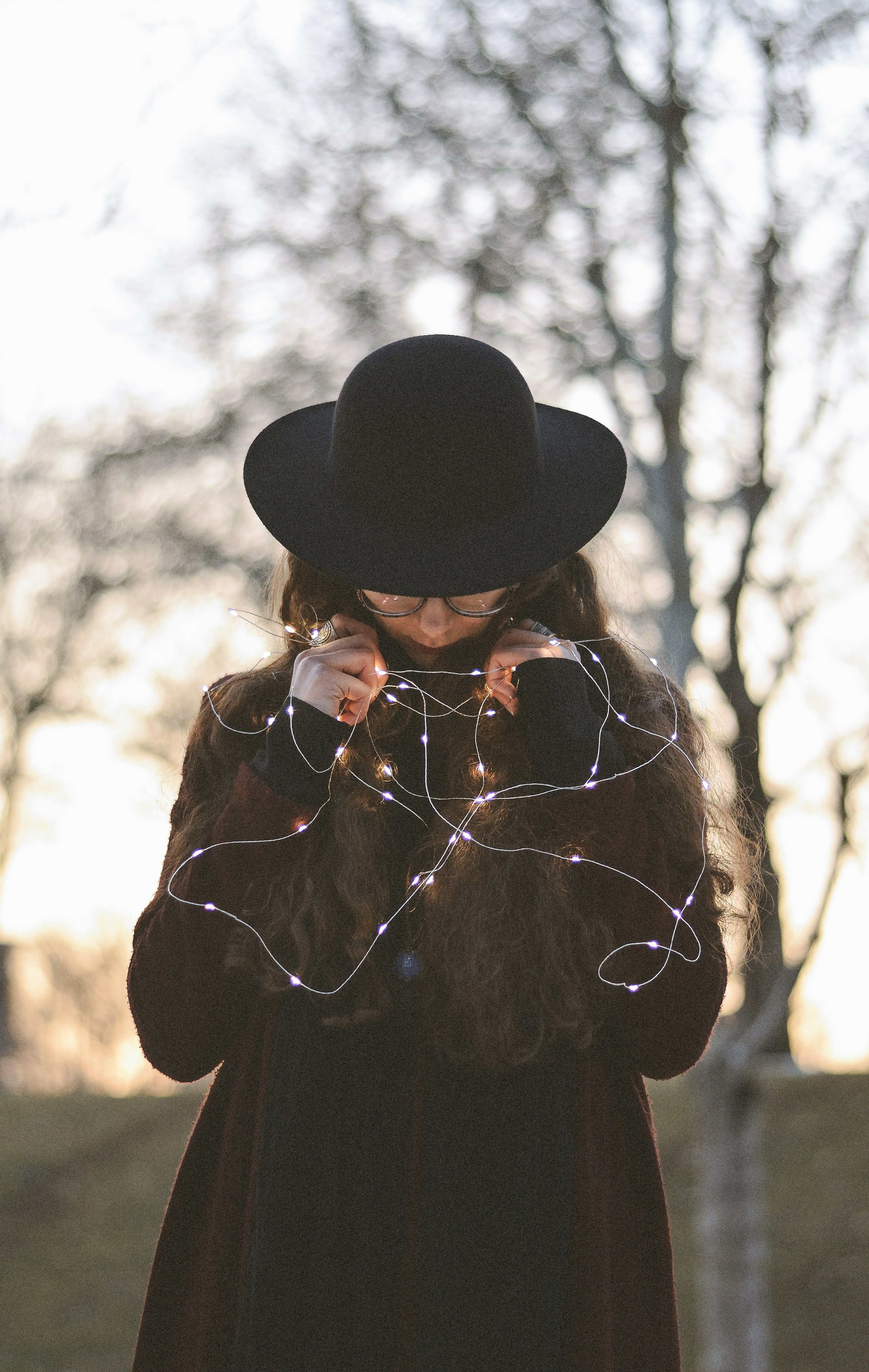 woman in black hat standing near bare trees during daytime