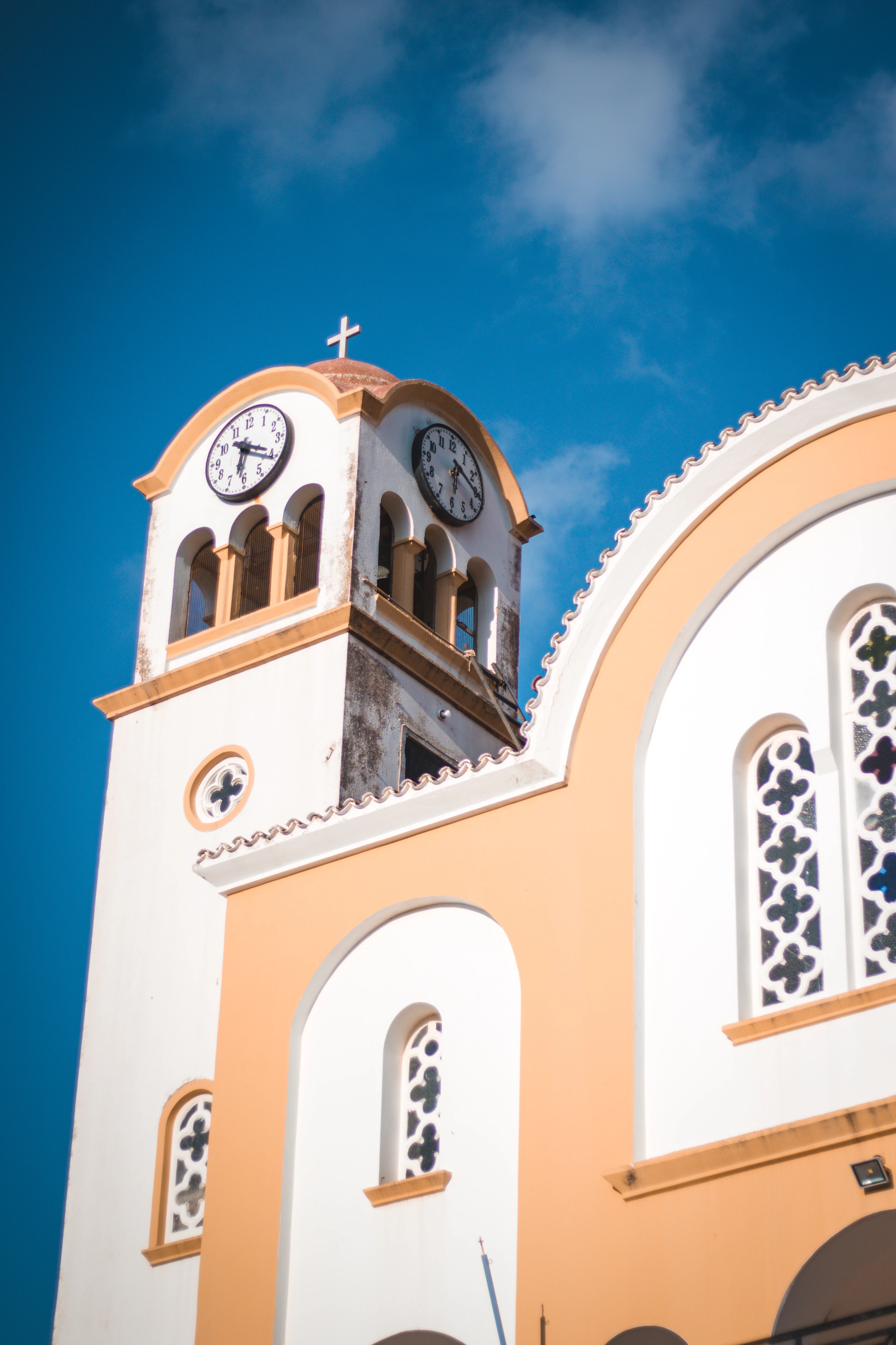 A whitewashed Greek Orthodox church bell tower with a clock face stands out against a vivid blue sky.