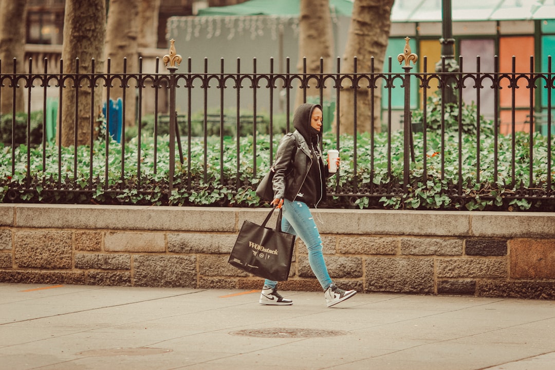 woman in black jacket and blue denim jeans with black sling bag walking on sidewalk during