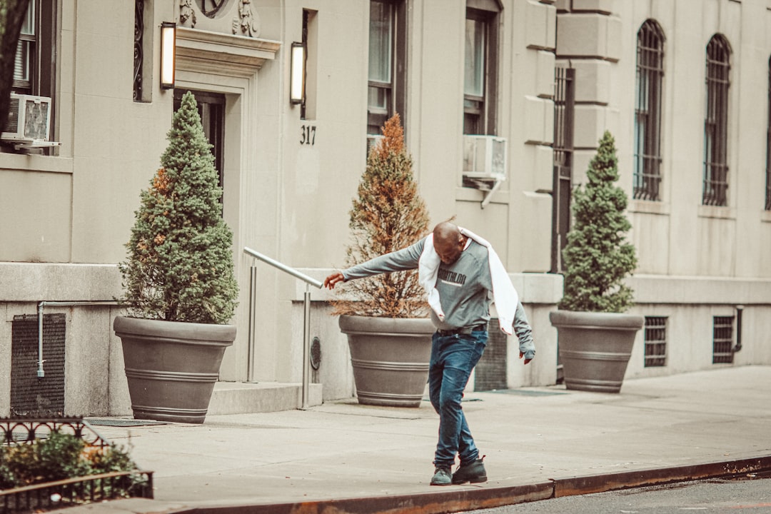 man in blue denim jacket and blue denim jeans holding stick walking on sidewalk during daytime