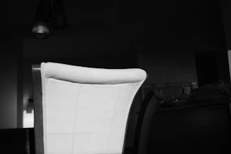 Monochrome image of a casual hoodie draped over a chair in a bright, airy room.