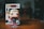 A Funko Pop figurine stands on a wooden surface. The figure has a superhero costume with a blue suit, red gloves, and boots. The character's blonde hair is stylized, and it is displayed in front of its original packaging box, which is slightly blurred in the background.