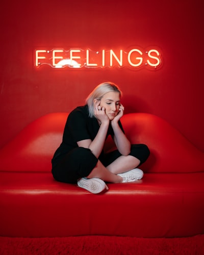 A girl sitting on a sofa under a neon feelings sign