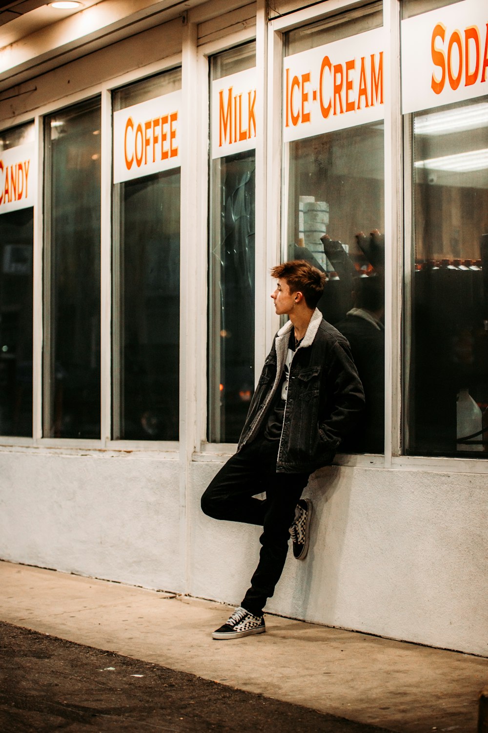 man in black suit jacket and black pants sitting on white concrete wall during daytime