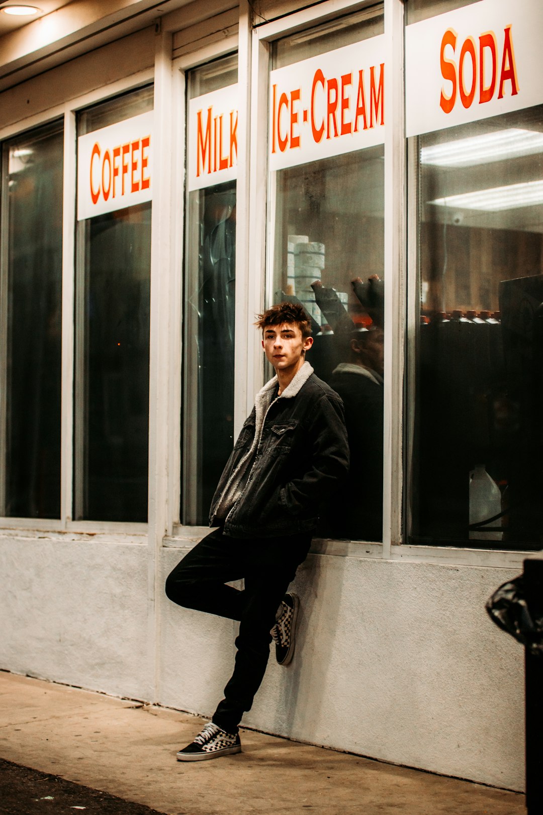 man in black leather jacket sitting on white concrete wall