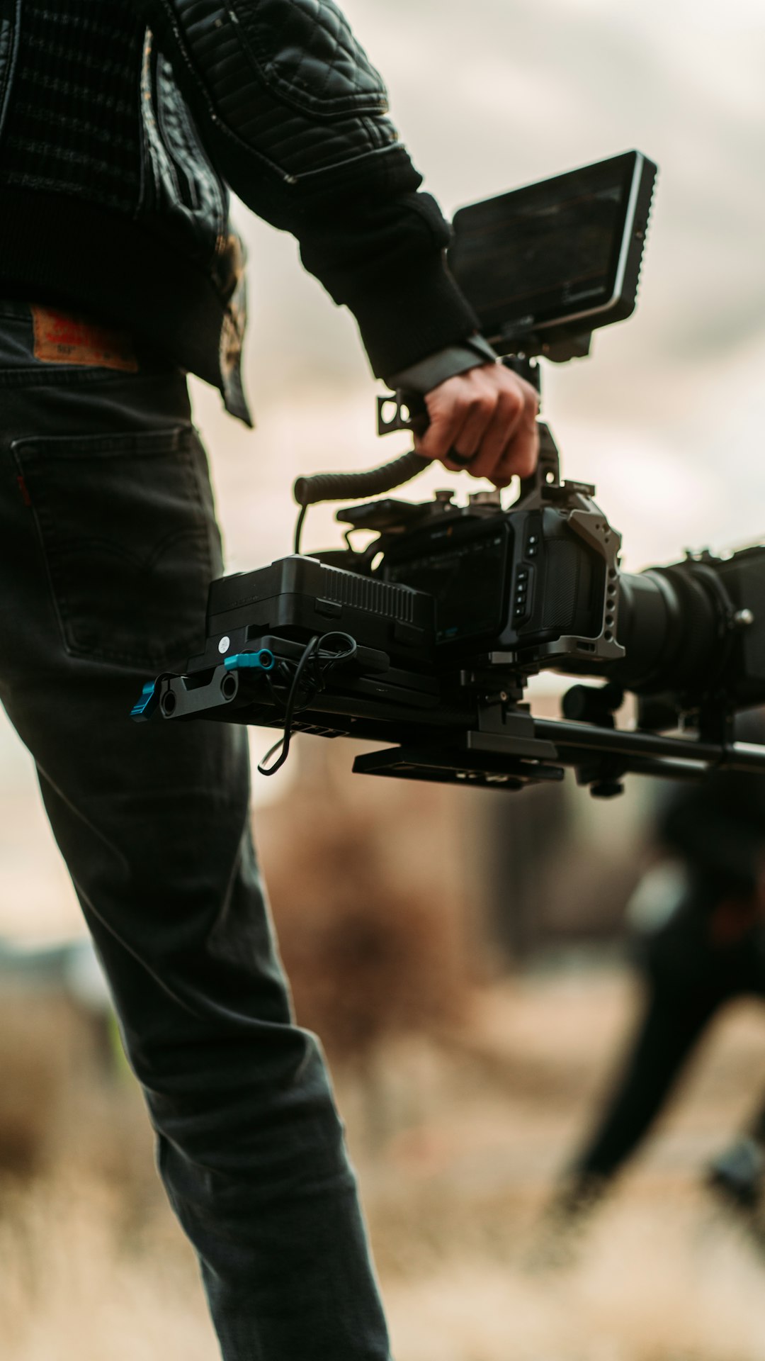 person in black jacket and blue denim jeans holding black video camera