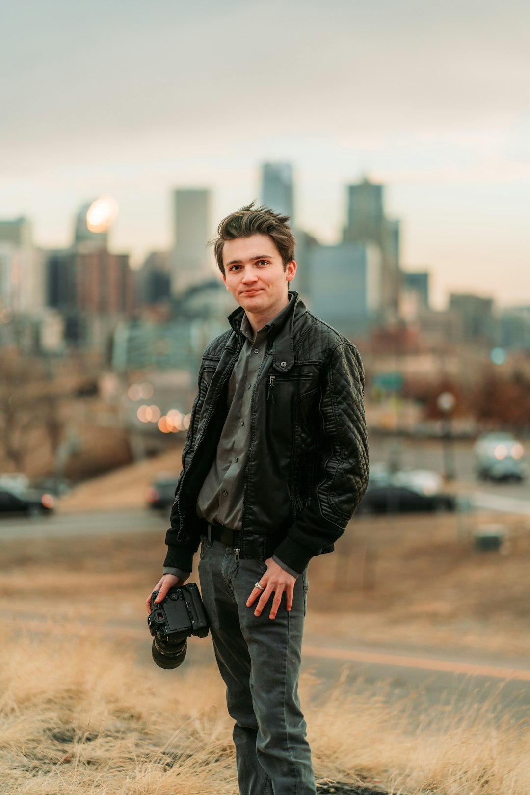 man in black leather jacket and gray pants holding black dslr camera