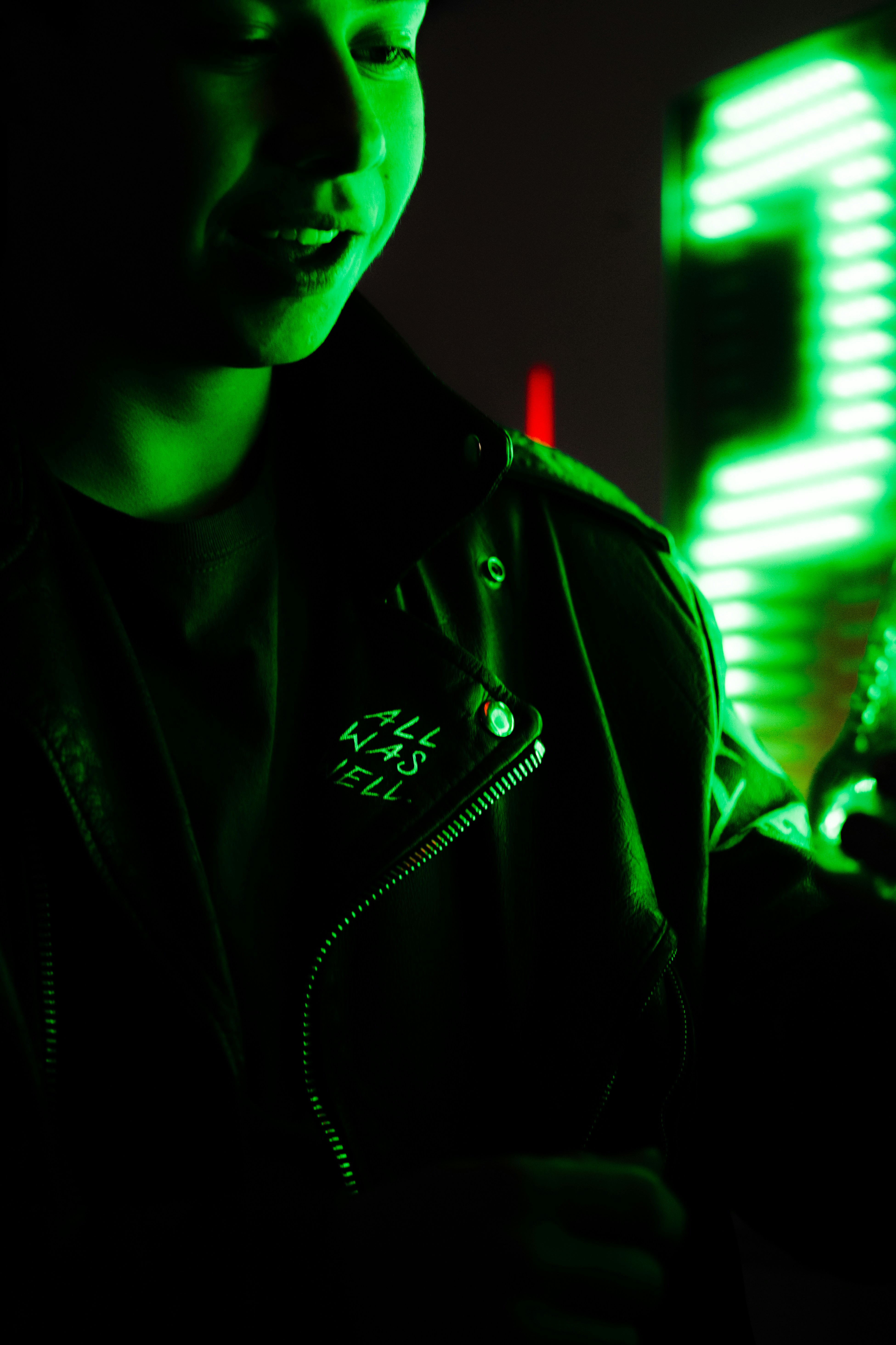 Man smiling slightly in dark environment with green neon light accent