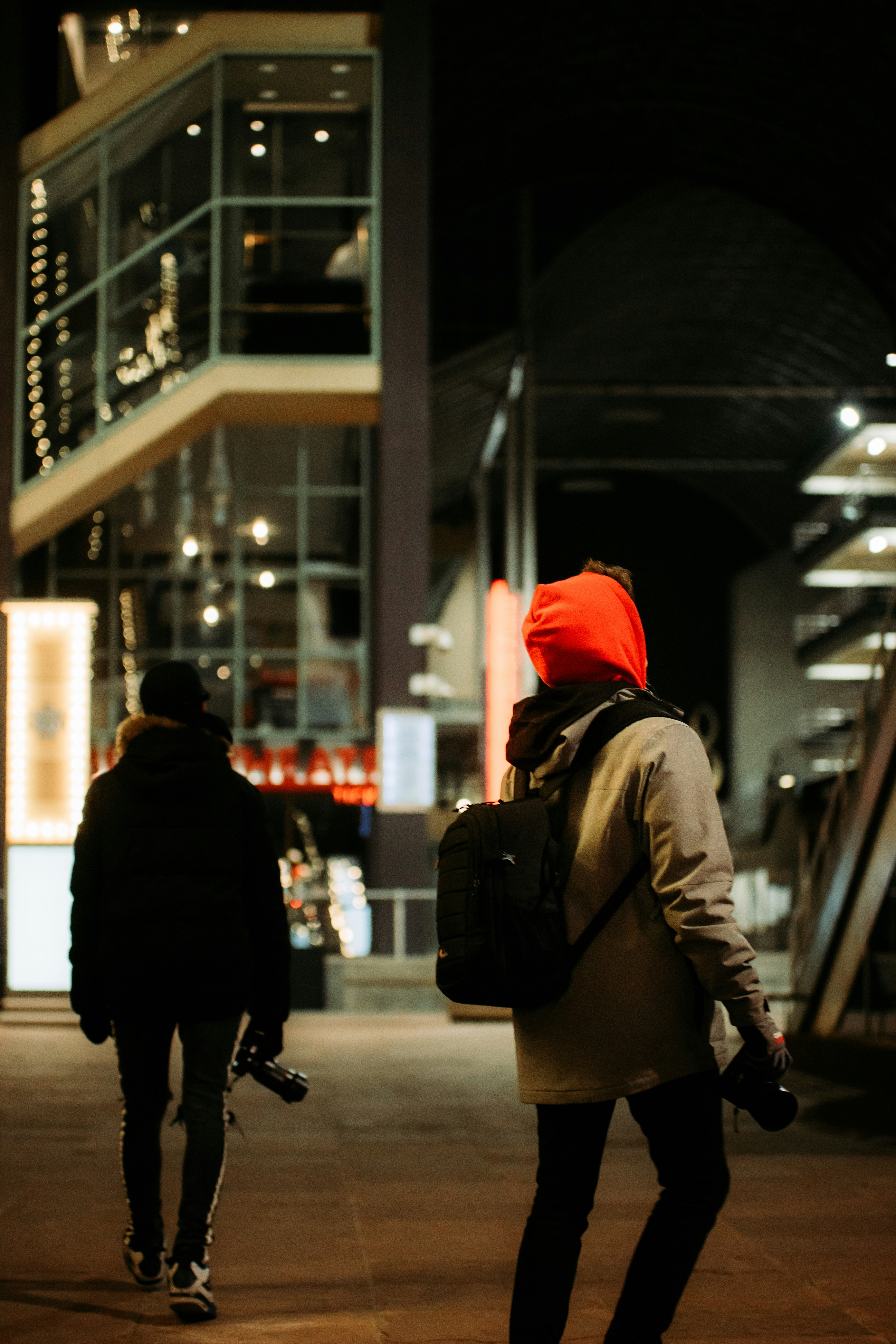 man in red knit cap and brown jacket walking on sidewalk during night time