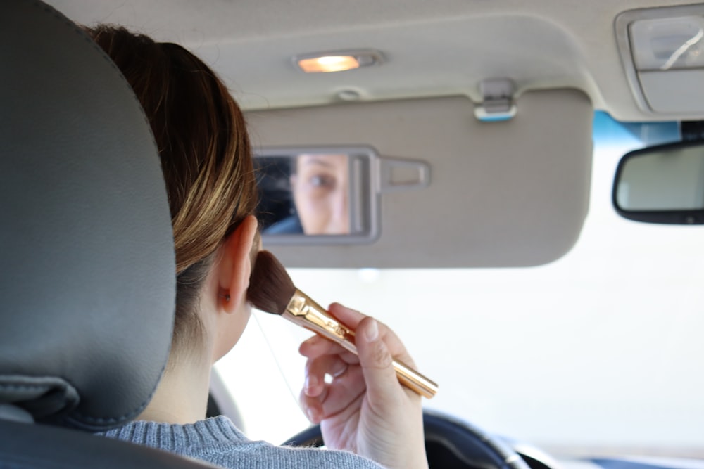 Mujer en suéter gris sosteniendo brocha de maquillaje marrón