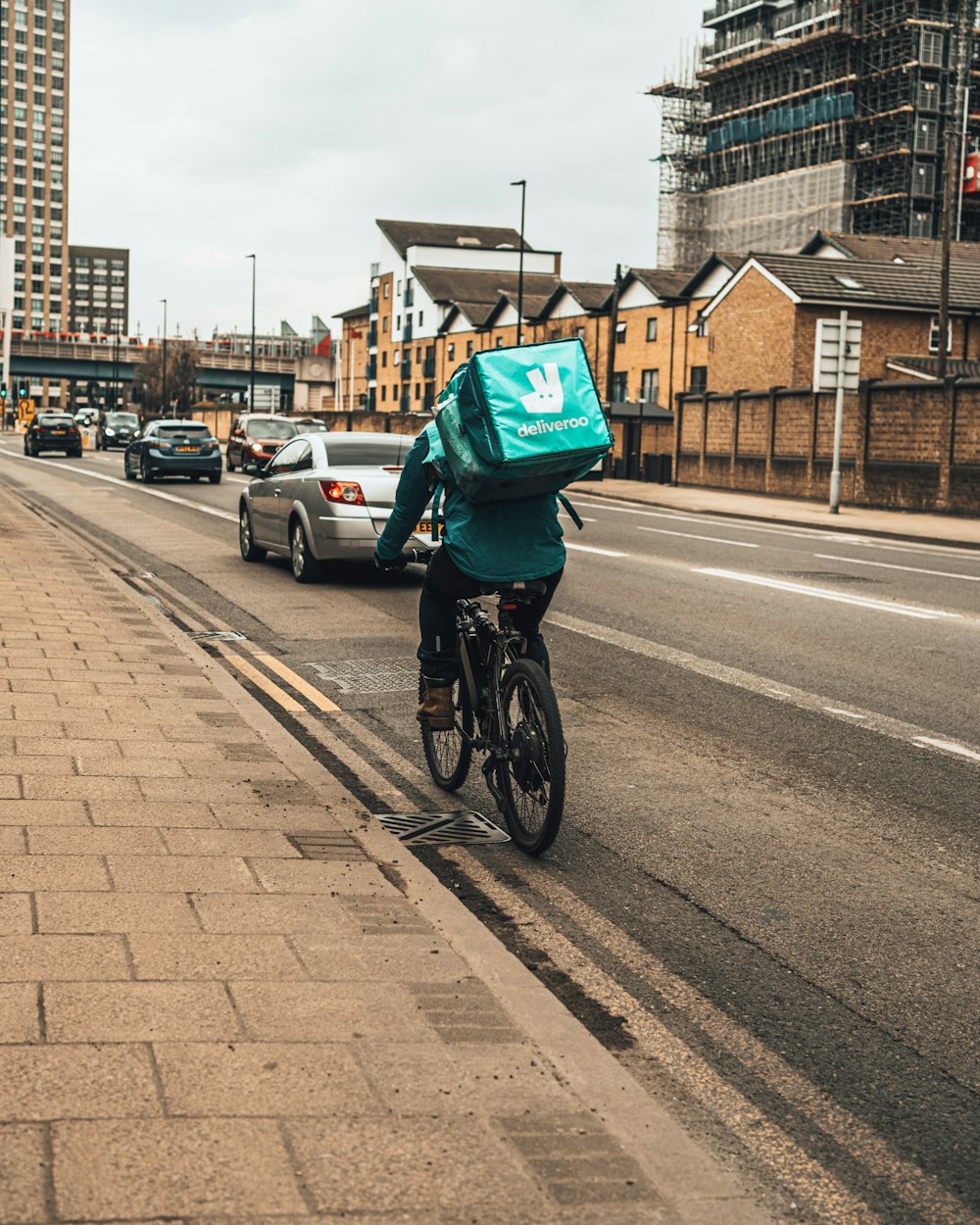 Persona in giacca verde che cavalca la bicicletta su strada durante il giorno