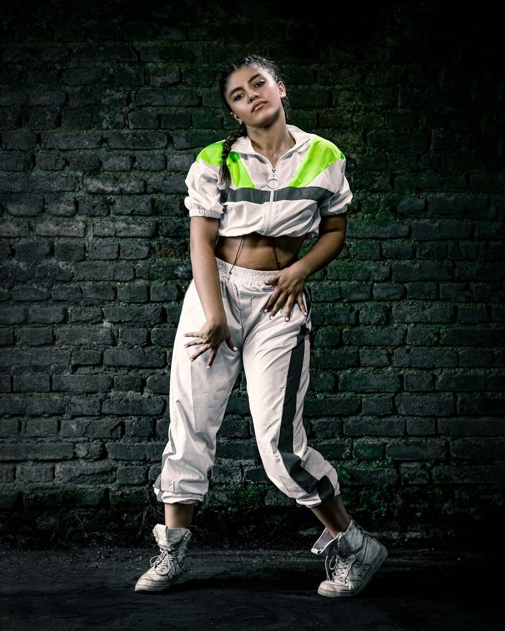 woman in white and green t-shirt and brown pants leaning on black brick wall
