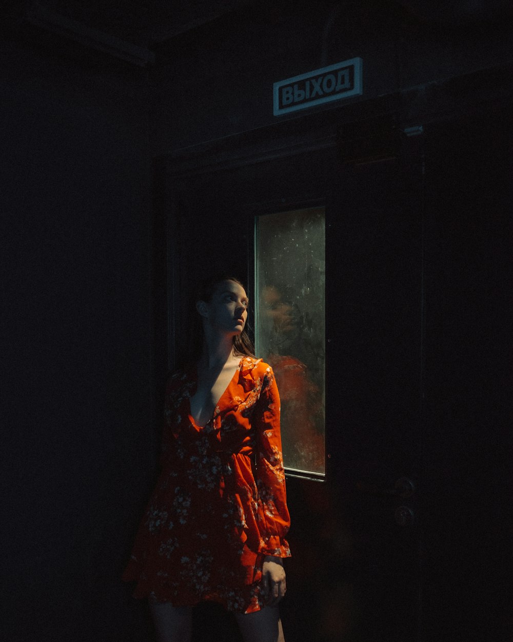 Mujer con vestido floral rojo y blanco de pie cerca de la puerta