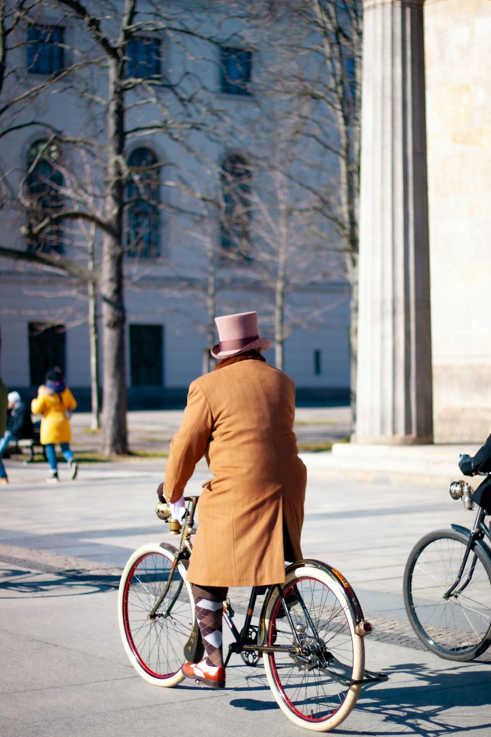 man in brown coat and black hat riding bicycle on road during daytime