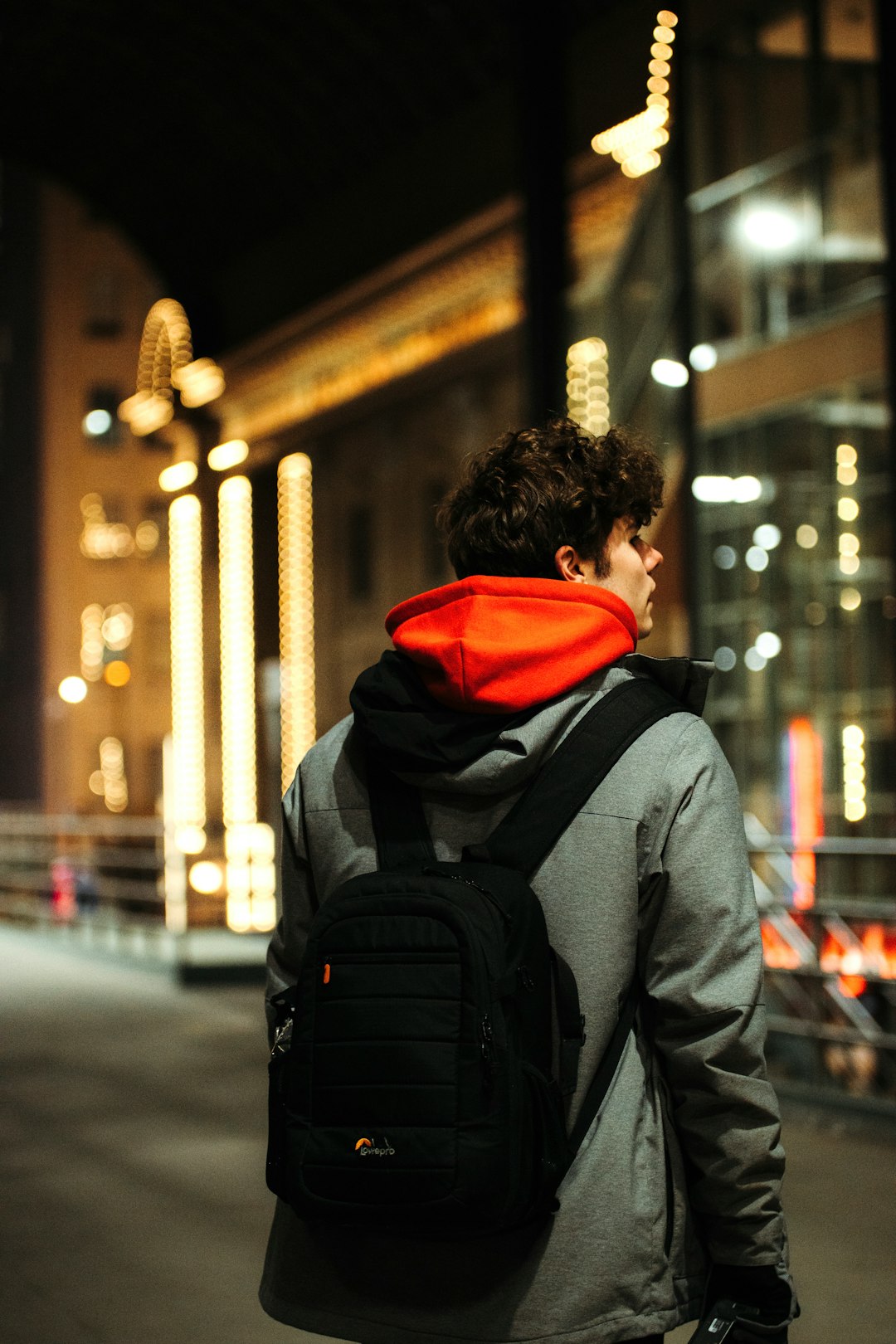 man in gray hoodie and red and black backpack standing on sidewalk during night time