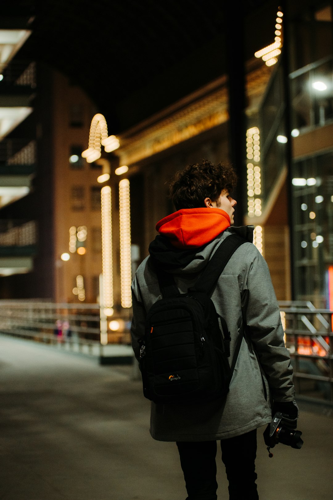 person in black and orange hoodie and black backpack walking on sidewalk during daytime