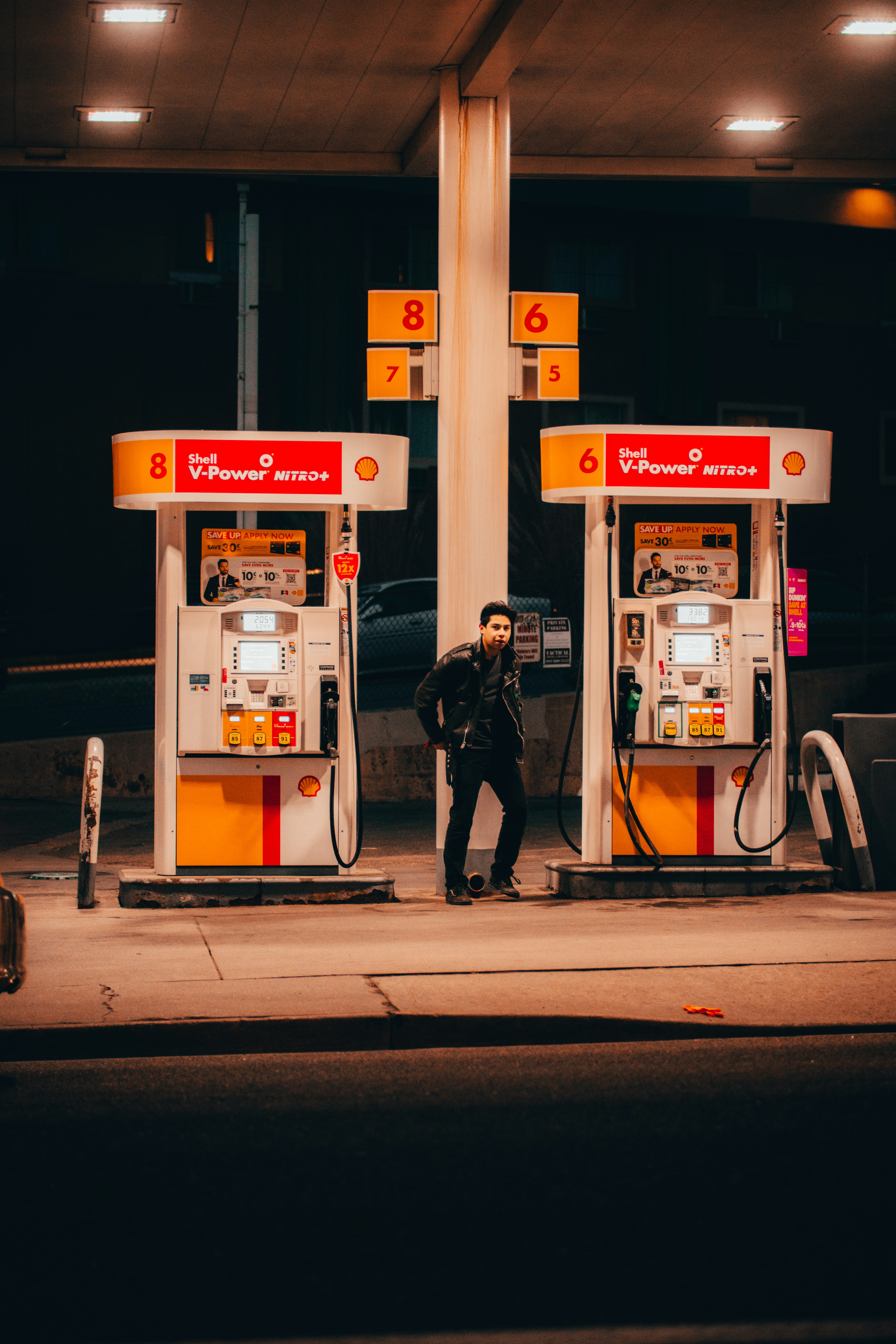 man in black jacket standing near white and red gas pump