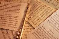 A silver flute is placed among several sheets of musical notation. The sheets feature complex arrangements and notes, spread out on a neutral background, suggesting a focus on music and practice.