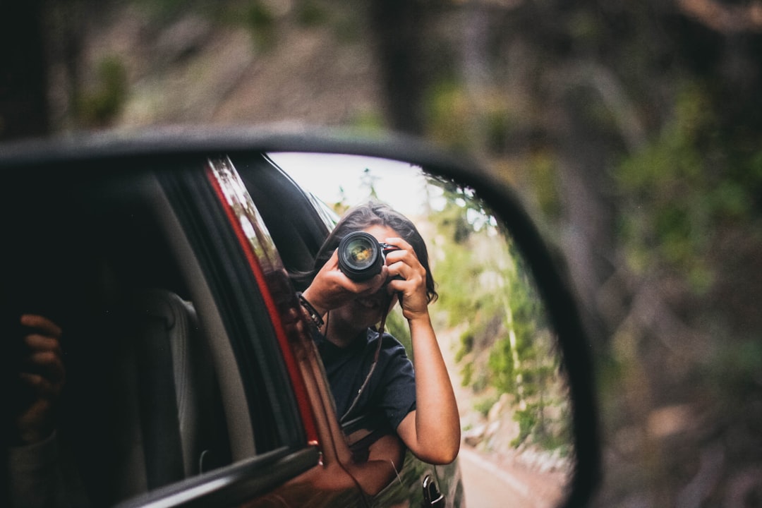 woman in brown t-shirt taking photo of car side mirror