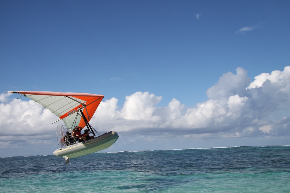 white and orange sail boat on sea under blue sky and white clouds during daytime