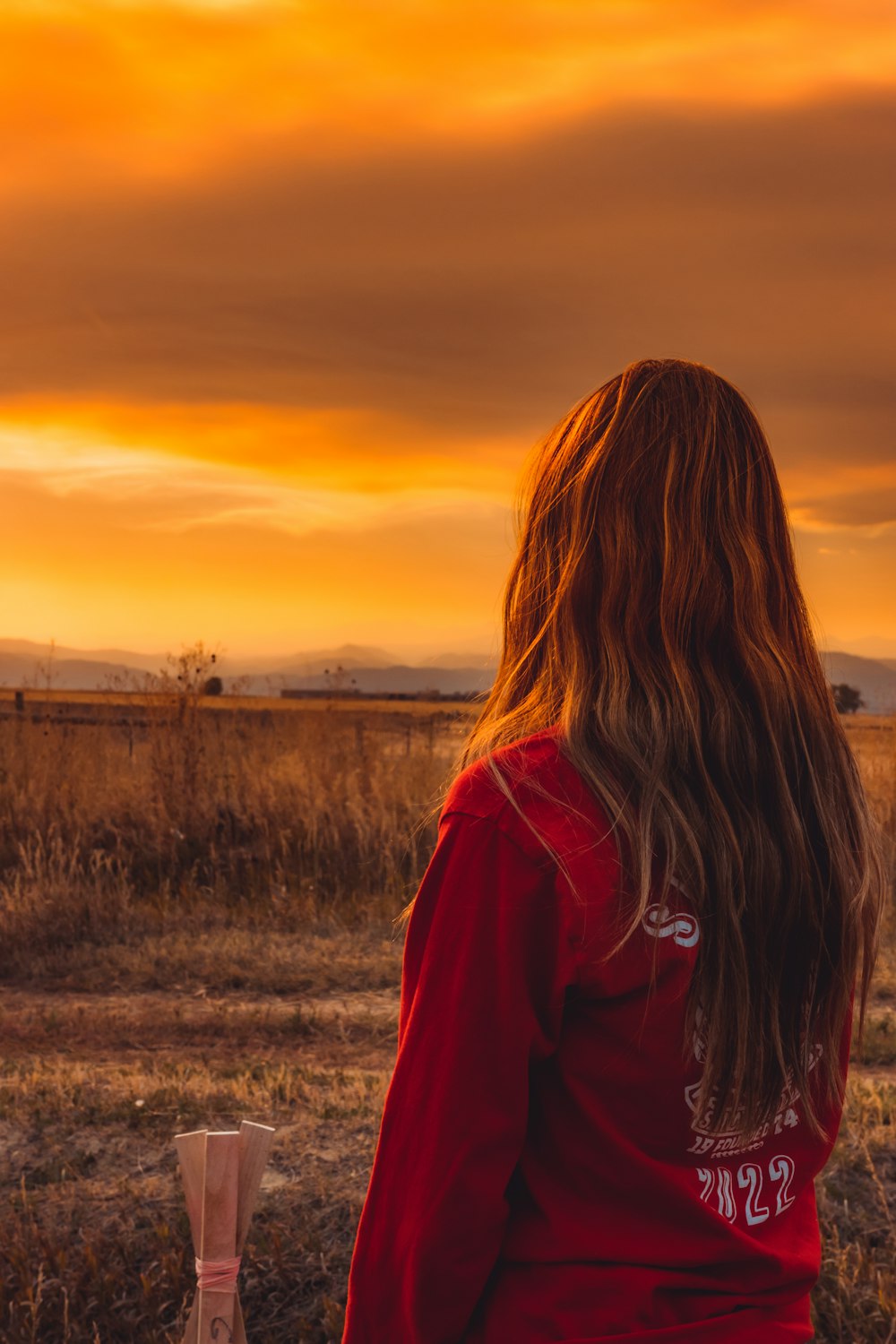 woman in red and black hoodie standing on grass field during sunset