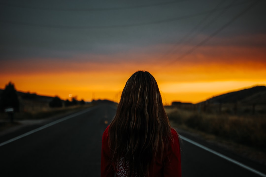 woman in red and black plaid shirt standing on road during sunset