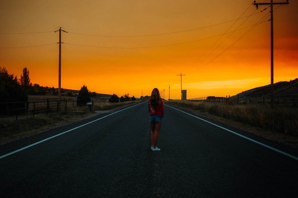 Femme en t-shirt bleu et short en jean bleu debout sur la route au coucher du soleil