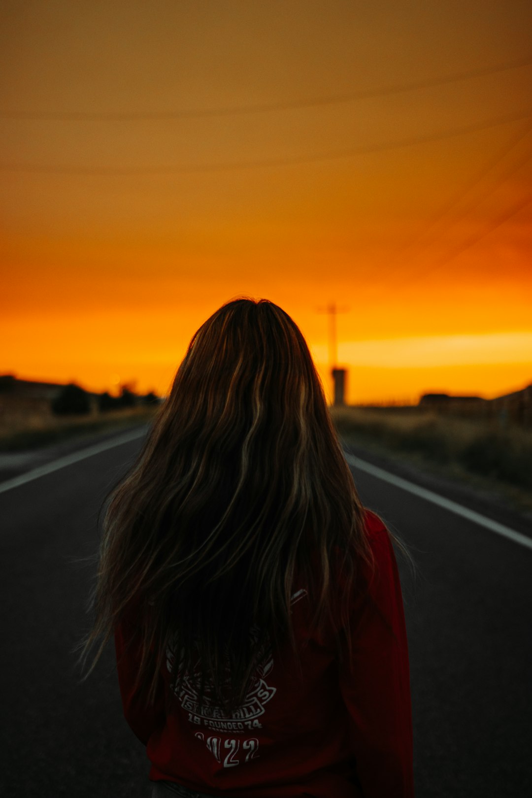 woman in red jacket standing on road during sunset