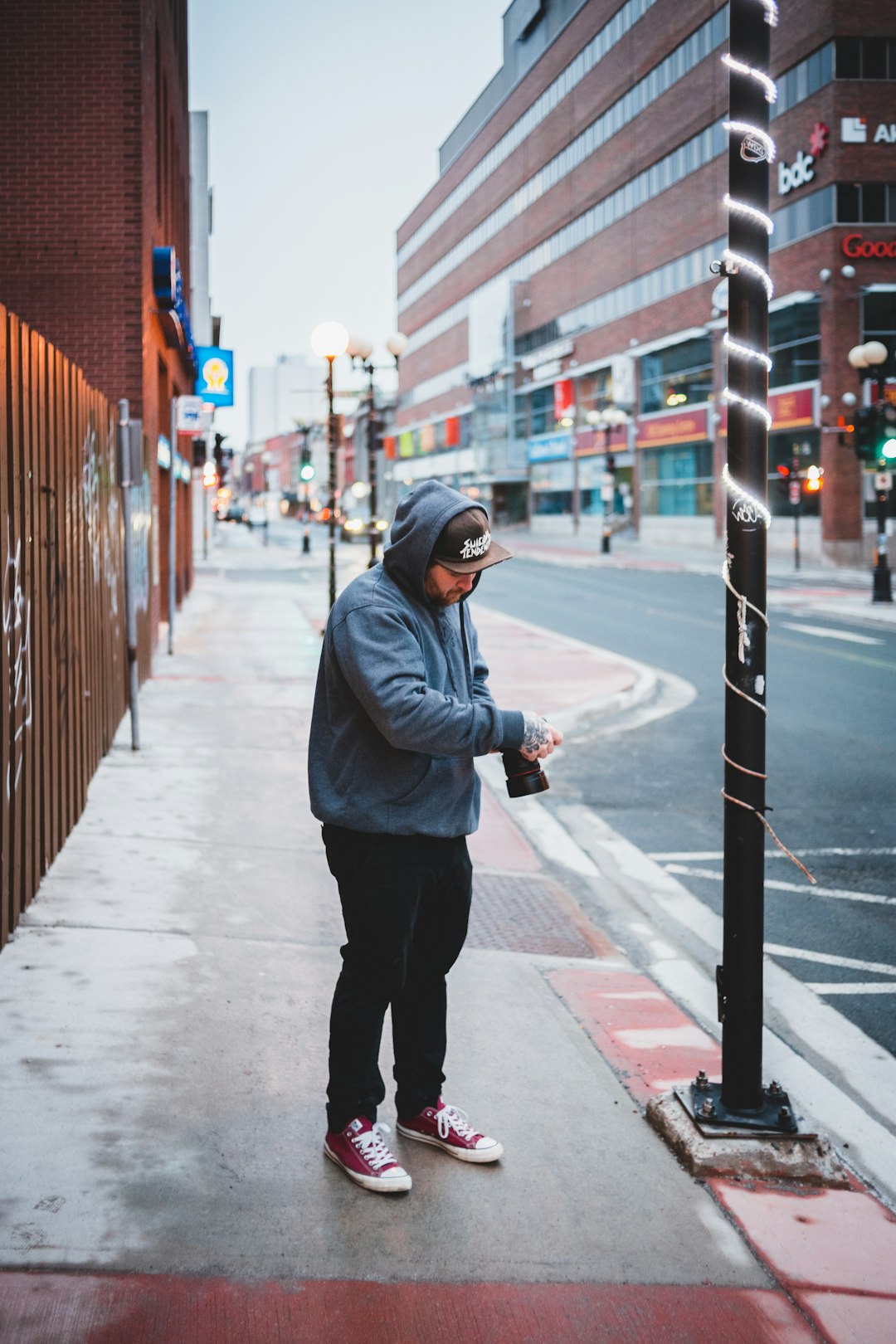 woman in gray hoodie and black pants standing on sidewalk during daytime