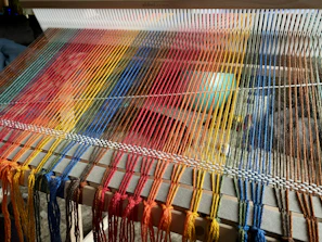 Close-up of hands weaving colorful yarn on a vintage loom in a sunlit studio