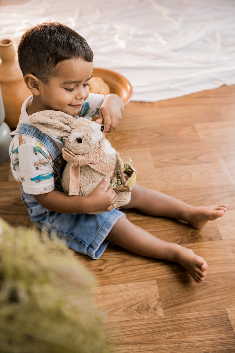 Niño en pantalones cortos de mezclilla azul sentado en el suelo sosteniendo un juguete de peluche de conejo blanco