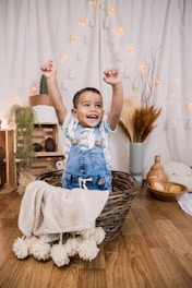 child in blue and white long sleeve shirt and blue denim dungaree on brown woven basket