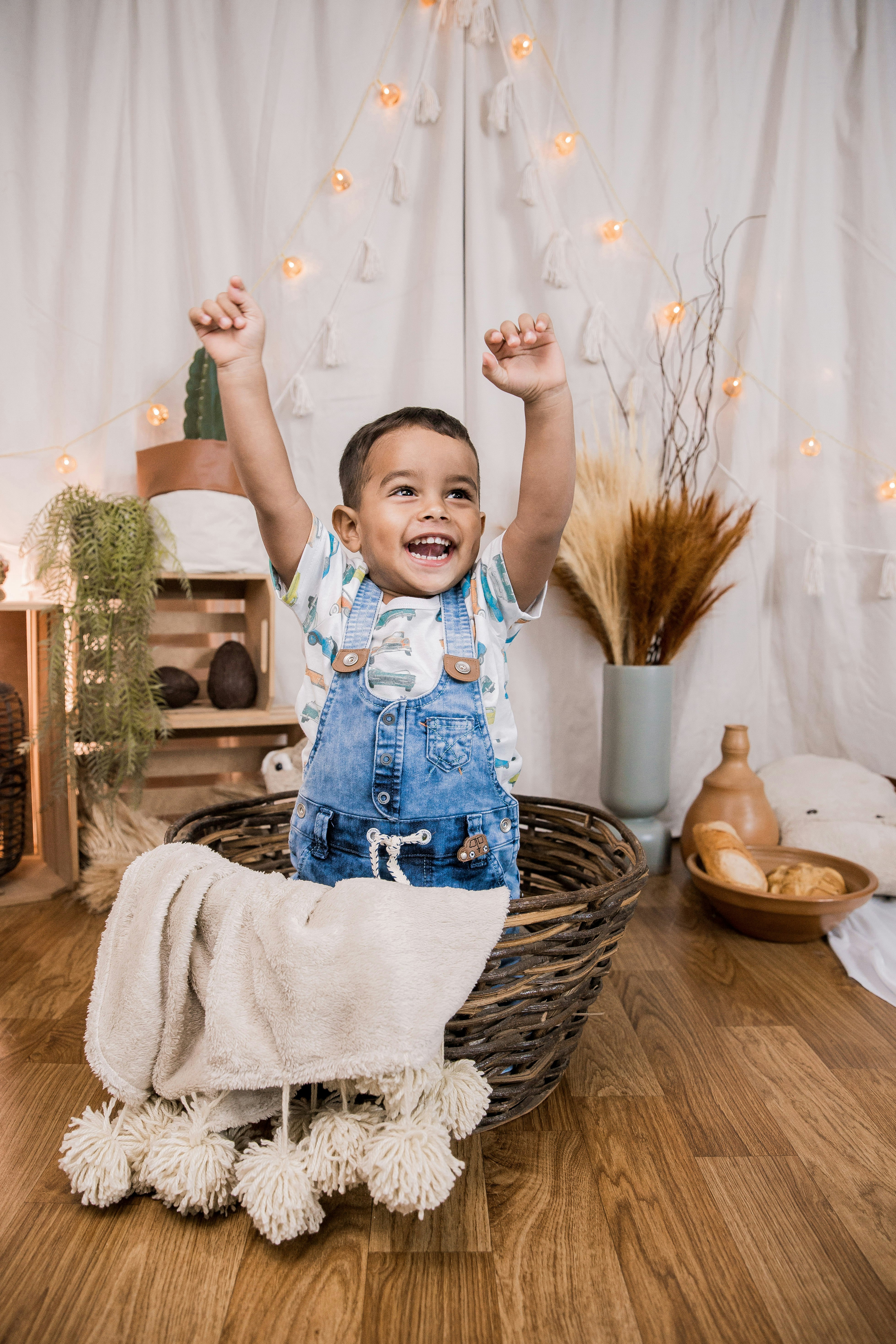 child in blue and white long sleeve shirt and blue denim dungaree on brown woven basket