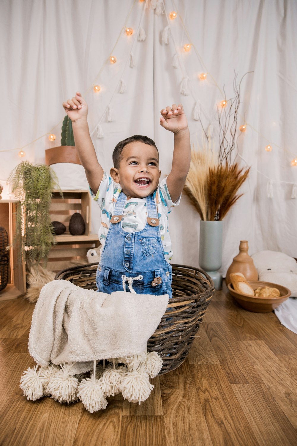 Niño con camisa de manga larga azul y blanca y peto de mezclilla azul sobre canasta tejida marrón