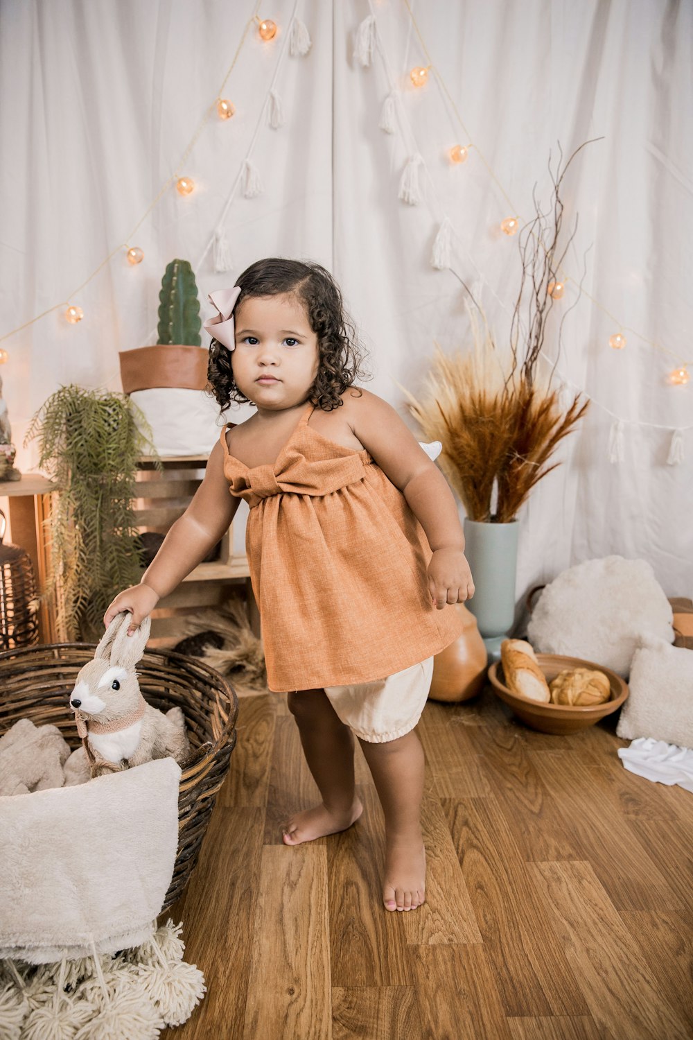 girl in pink dress standing beside white dog on brown wicker basket