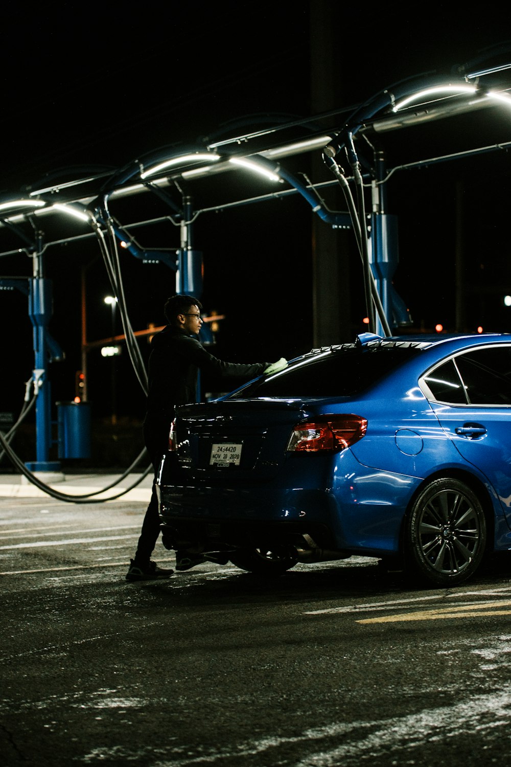 man in black jacket standing beside blue car