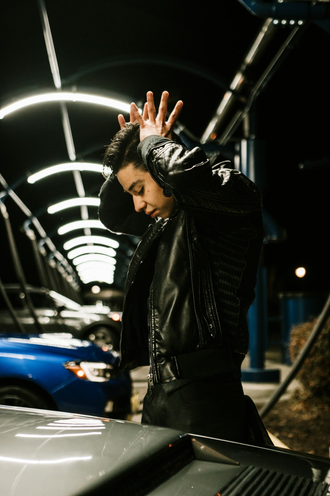 woman in black leather jacket standing beside blue car