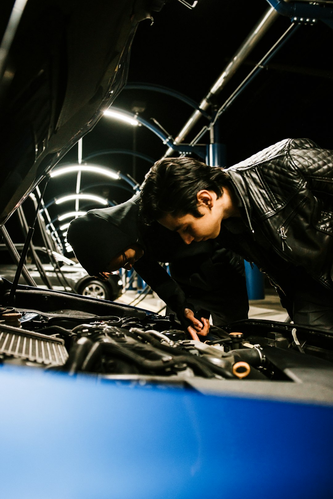 man in black leather jacket and blue denim jeans sitting on black and silver car engine
