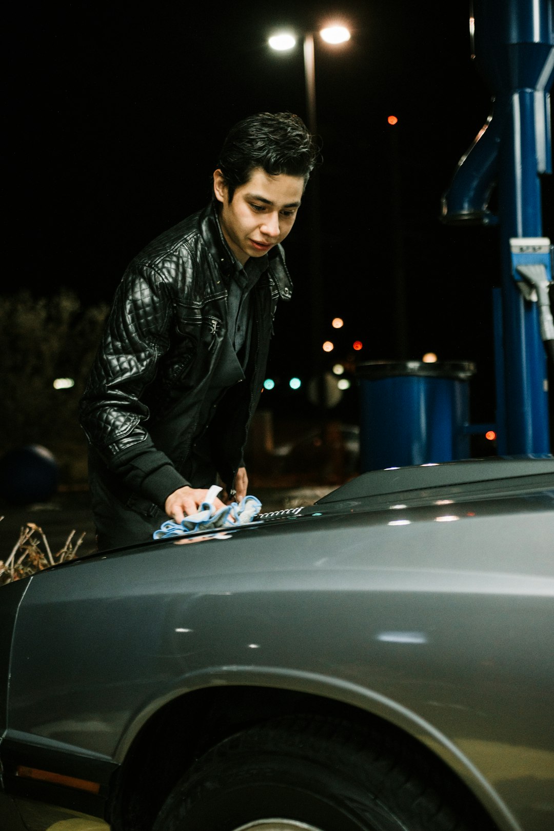 man in black leather jacket leaning on black car