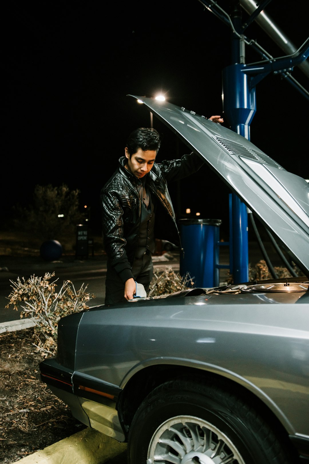 man in black leather jacket standing beside silver car during night time