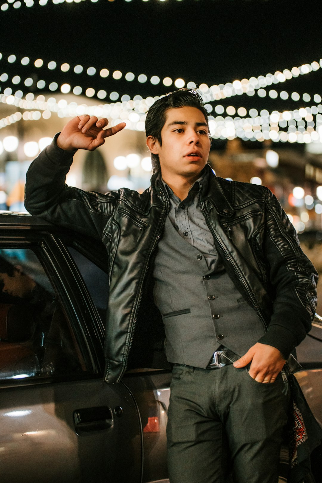 man in black leather jacket standing beside black car during night time