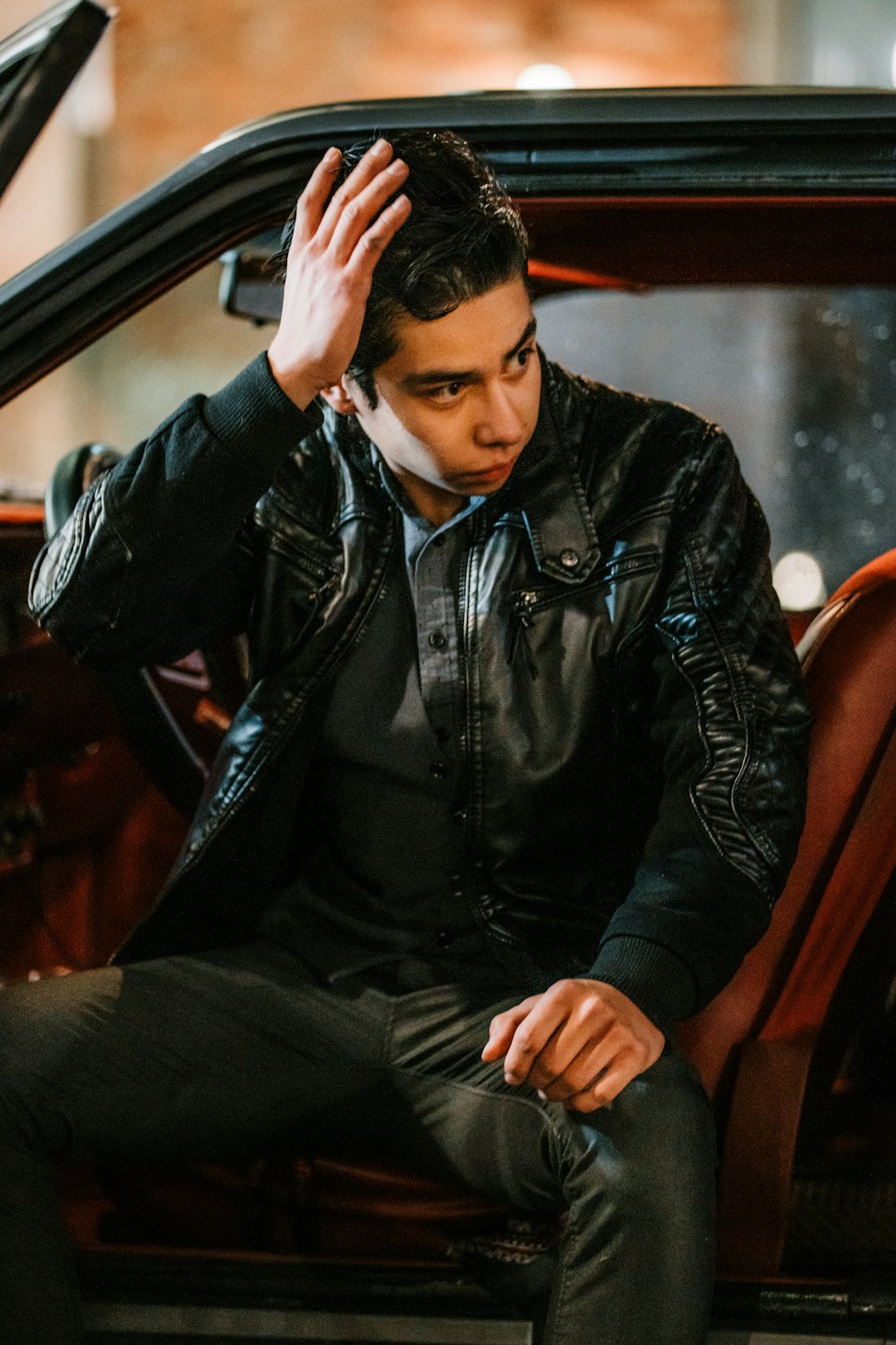 man in black leather jacket sitting on brown wooden chair