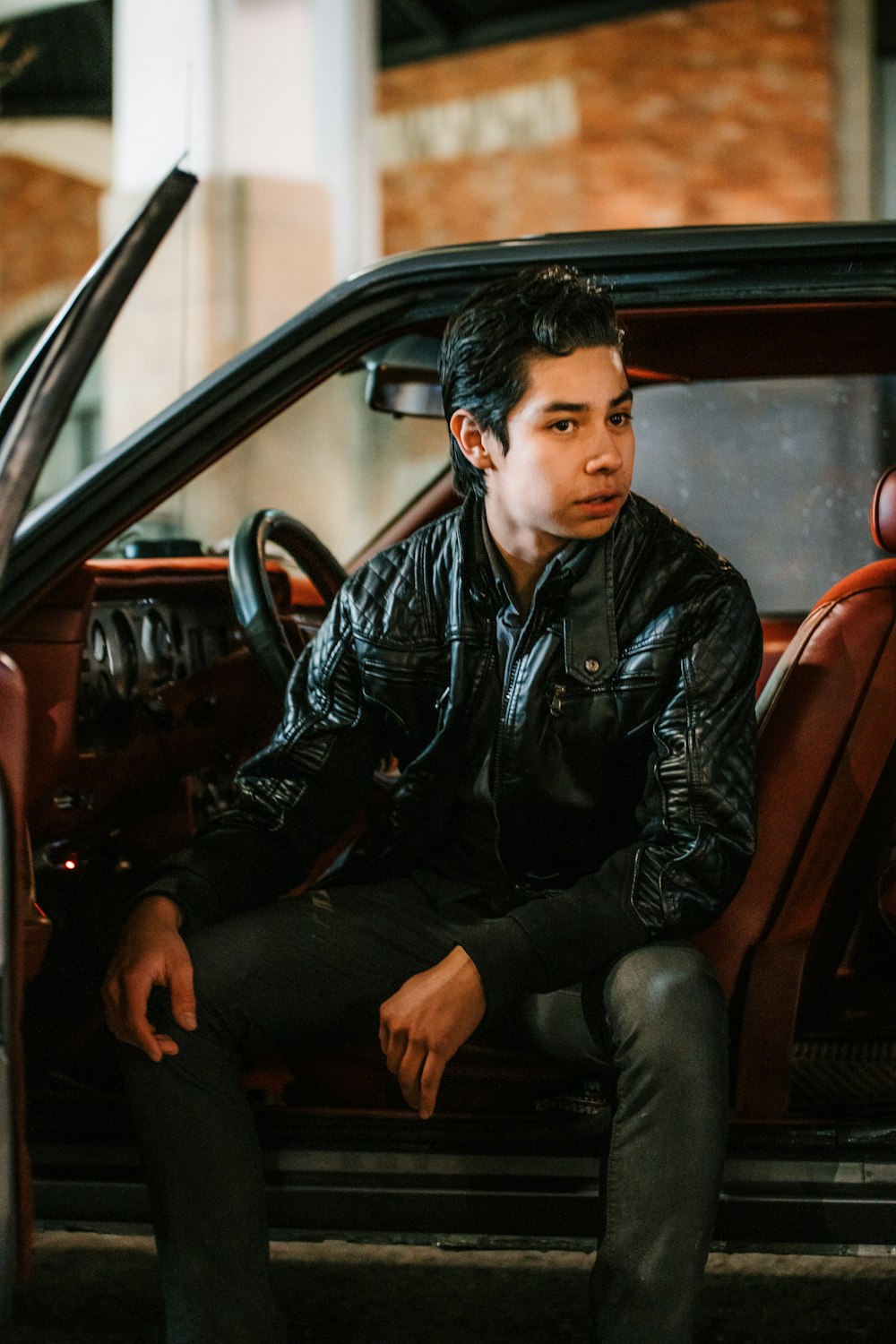 man in black leather jacket sitting on red car seat