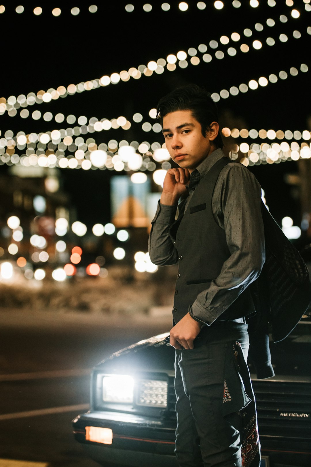 man in black jacket and blue denim jeans standing on road during night time