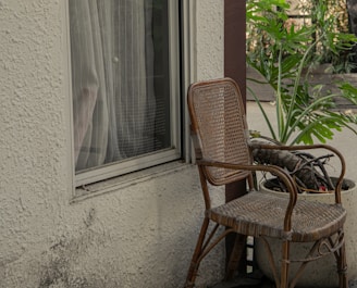 A simple wooden rocking chair beside a window with potted sage and clay pots.