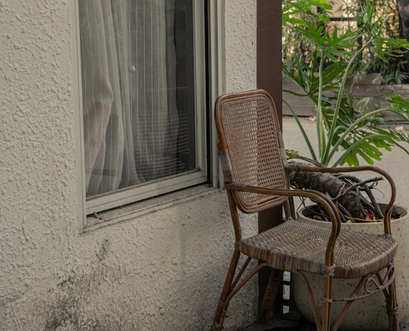 A simple wooden rocking chair beside a window with potted sage and clay pots.
