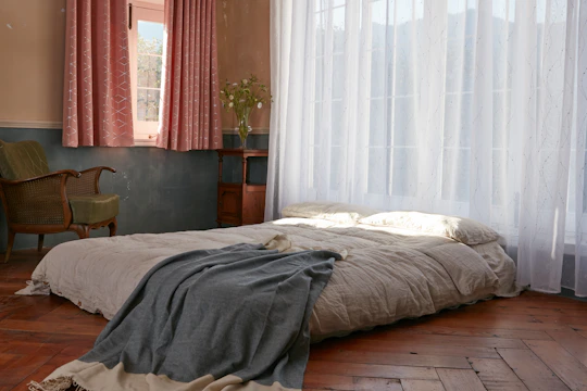 Cozy bedroom with low wooden bed frame, cream linen sheets, and soft gray stone accent wall.