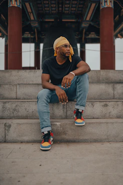 man in black crew neck t-shirt and blue denim jeans sitting on gray concrete stairs