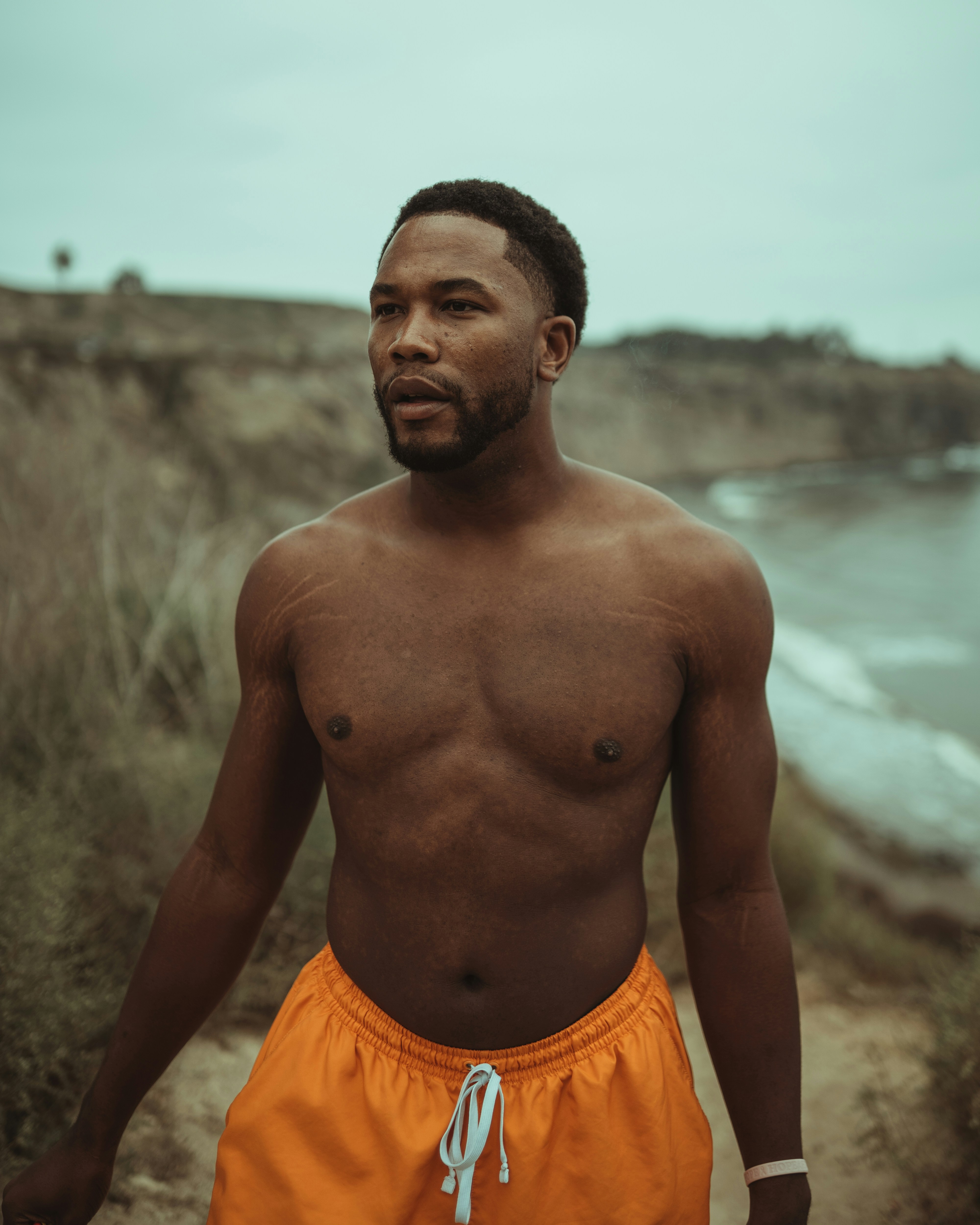 Topless man in orange shorts standing near body of water during daytime