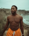 topless man in orange shorts standing near body of water during daytime